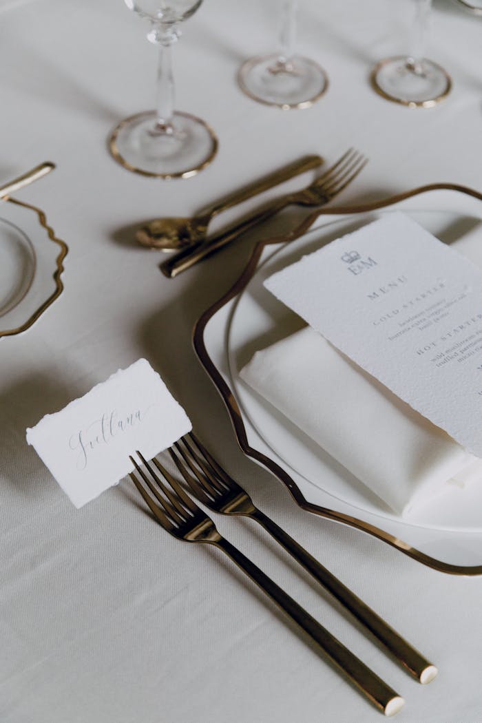 A sophisticated wedding table setting featuring fine cutlery, wine glasses, and a detailed menu on a white tablecloth.