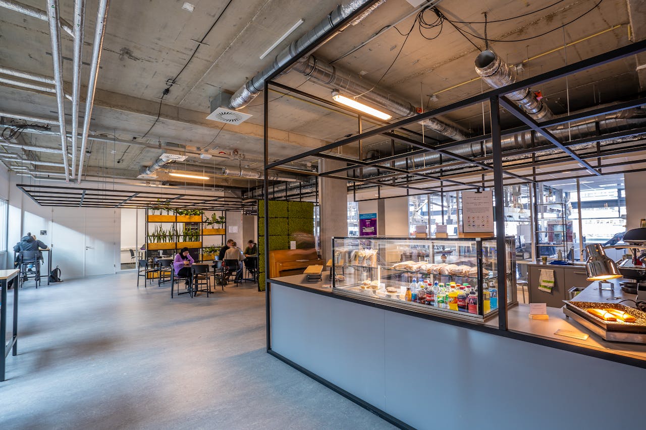 our-story-01 A spacious modern cafeteria with industrial design, showcasing people dining and working in a relaxed atmosphere.